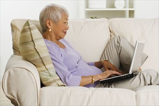 Senior Asian woman using laptop on sofa