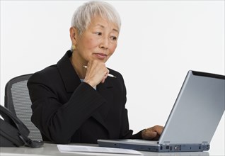 Senior Asian businesswoman using laptop at desk