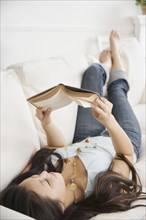 Asian woman laying on sofa reading