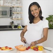 Pregnant African woman chopping fruit