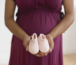 Pregnant African woman holding baby shoes