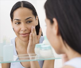 African woman applying face cream in mirror