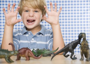Young boy making face with toy dinosaurs