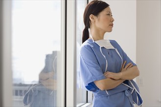Asian female doctor leaning against window with arms crossed