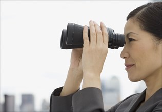 Profile of Asian businesswoman looking through binoculars
