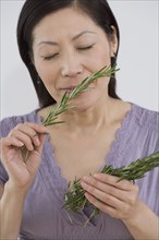Middle-aged Asian woman with eyes closed smelling springs of rosemary