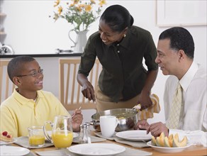 African woman serving breakfast to husband and son