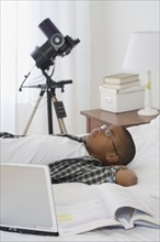 African boy laying on bed next to laptop and school books