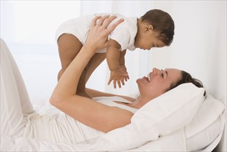 Hispanic mother playing with baby on bed