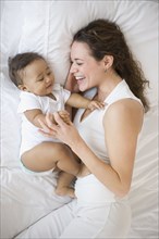 Hispanic mother playing with baby on bed