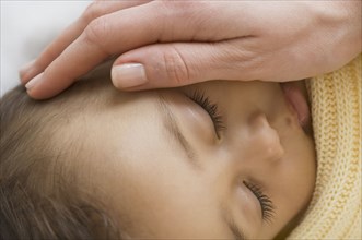 Close up of Hispanic sleeping baby with mother's hand on cheek