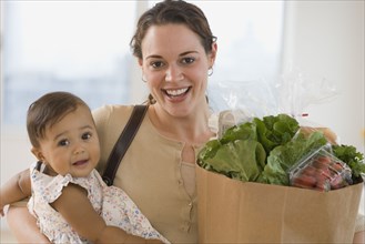 Hispanic mother carrying baby and groceries