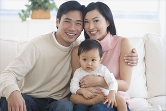 Asian parents holding baby on sofa