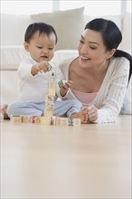 Asian mother and baby playing with blocks on floor