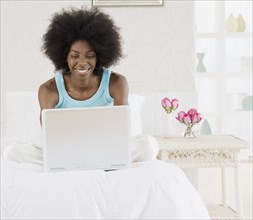 African woman using laptop on bed