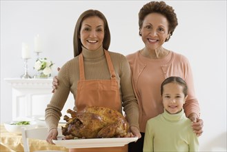 Multi-generational Hispanic family holding roast turkey