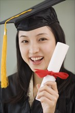 Asian woman wearing graduation cap and holding diploma
