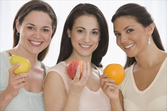 Three young women holding fruit