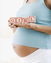 Pregnant African American woman holding 'GIRL' blocks