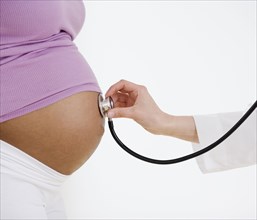 Doctor holding stethoscope on pregnant woman's belly