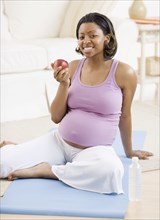 Pregnant African American woman eating apple