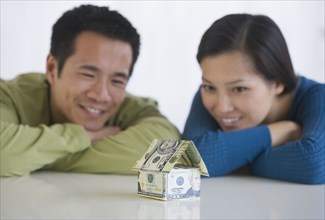 Asian couple looking at house made of money