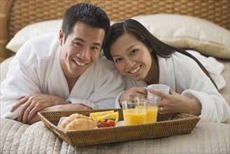 Asian couple eating breakfast in bed