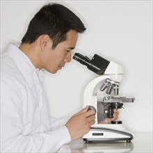 Asian male scientist looking into microscope