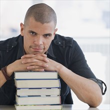 Hispanic man resting chin on stack of books