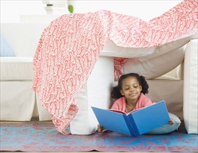 Mixed race girl reading in living room fort