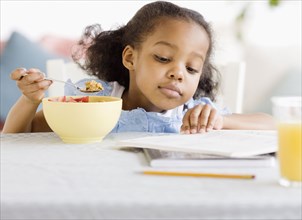 Mixed race girl reading and eating breakfast