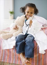 Mixed race girl playing doctor with teddy bear