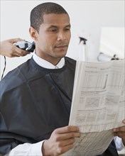 African man reading paper at barbershop
