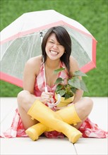 Asian woman sitting underneath umbrella in rain