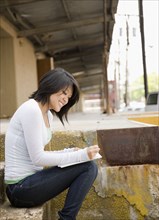Asian woman writing and sitting on loading dock
