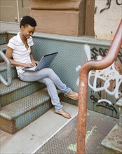 African woman sitting on urban steps with laptop