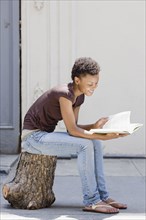 African woman sitting on tree stump and reading