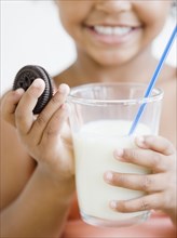Mixed race girl holding glass of milk and cookie