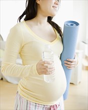 Pregnant Asian woman carrying yoga mat and water