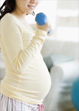 Pregnant Asian woman lifting dumbbells