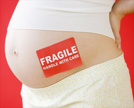 Pregnant Asian woman with fragile sticker on stomach