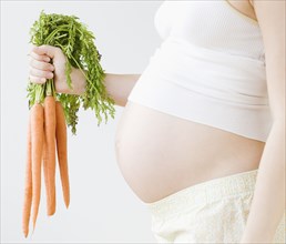 Pregnant Asian woman holding bunch of carrots