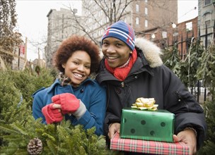 African couple in Christmas tree lot holding presents