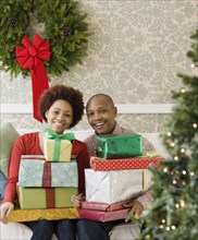 African couple in living room holding stacks of Christmas presents