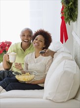 African couple watching television with popcorn and hot chocolate