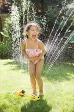 Hispanic girl playing in water sprinkler