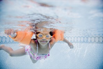 Hispanic girl swimming underwater in pool
