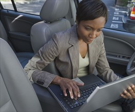 African businesswoman typing on laptop in car