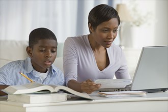 African boy doing homework next mother on computer