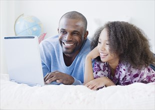 African father and daughter using laptop on bed